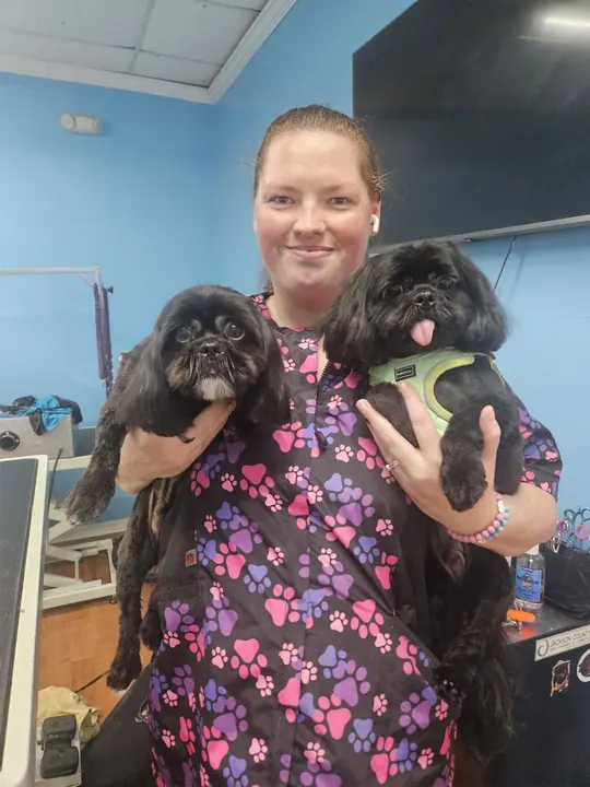 Smiling groomer holding two freshly groomed small dogs